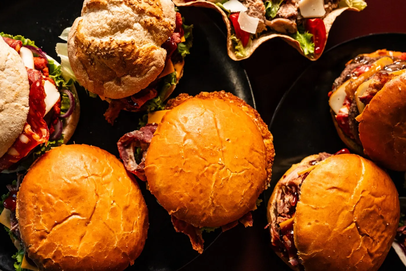 Cinque hamburger di Mr. Smoky su un vassoio nero, con pane artigianale e bacon
